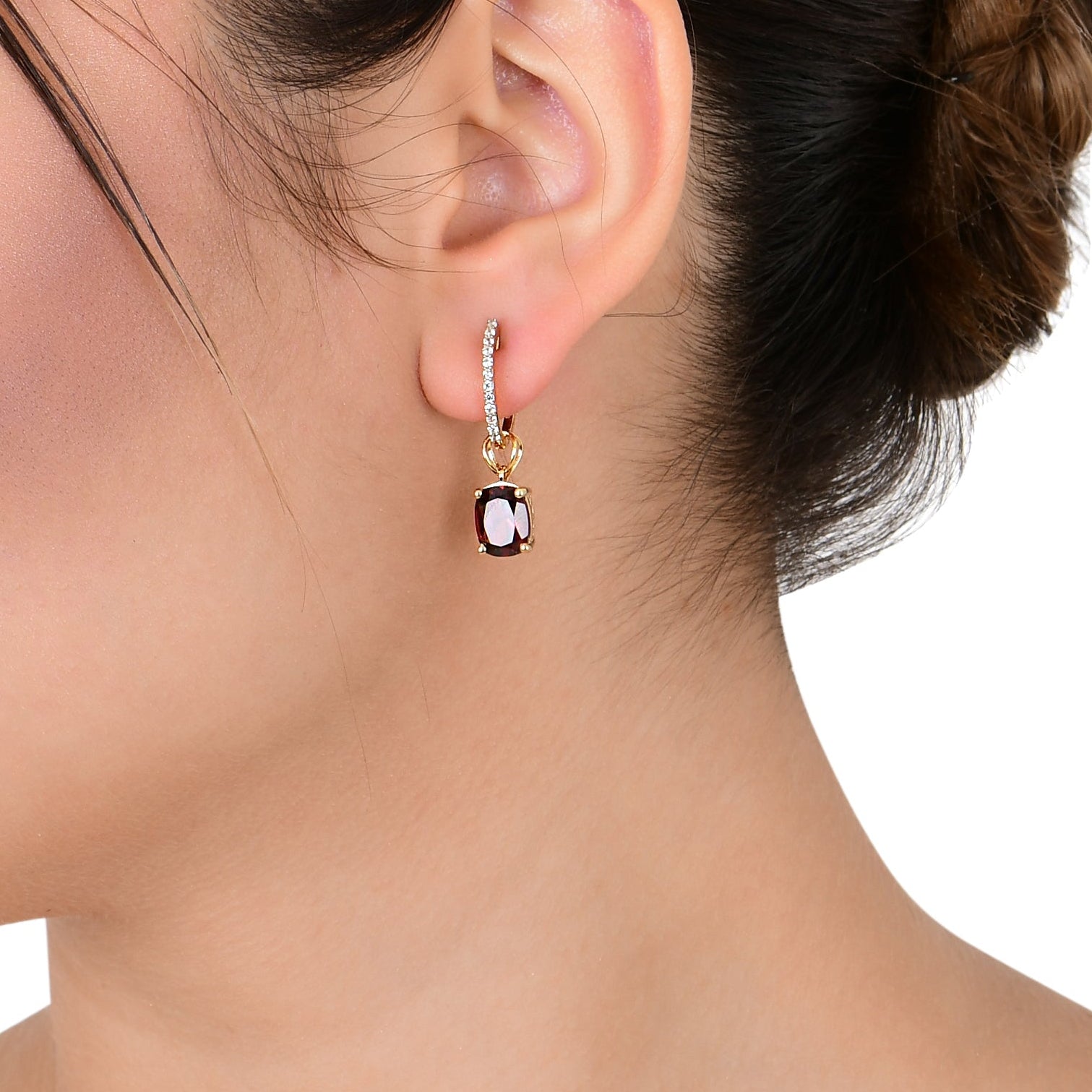 Woman wearing a gold earring with a black gemstone on a white background