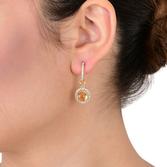 Woman wearing a gold earring with a gemstone on a white background
