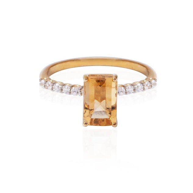 Gold ring with a rectangular citrine stone and diamond-studded band on a white background