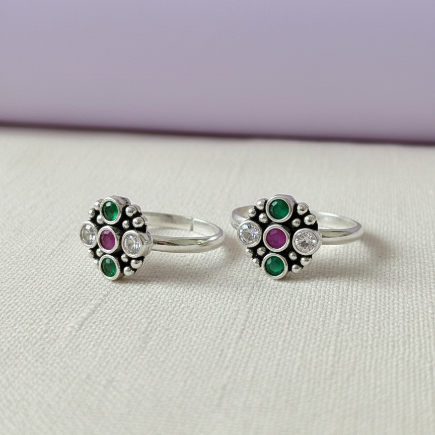 Pair of silver rings with green and purple gemstones on a light gray background