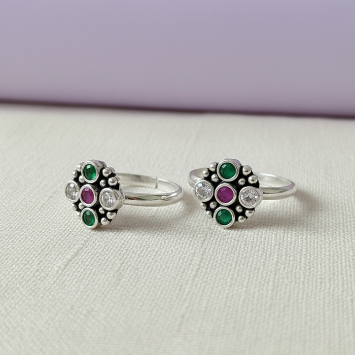 Pair of silver rings with green and purple gemstones on a light gray background