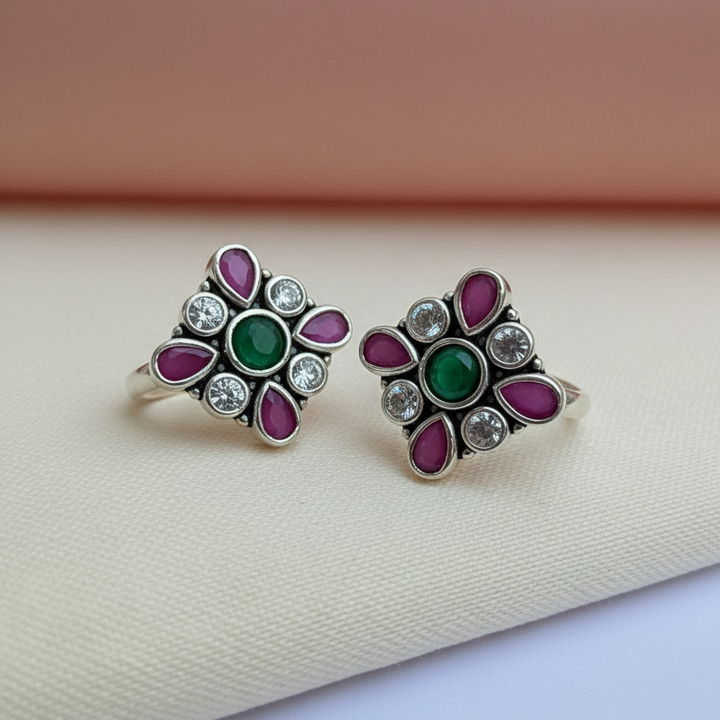 Pair of silver earrings with green and purple gemstones on a beige fabric background