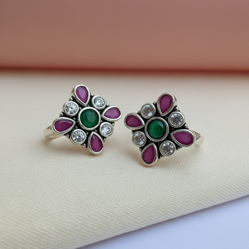 Pair of silver earrings with green and purple gemstones on a beige fabric background