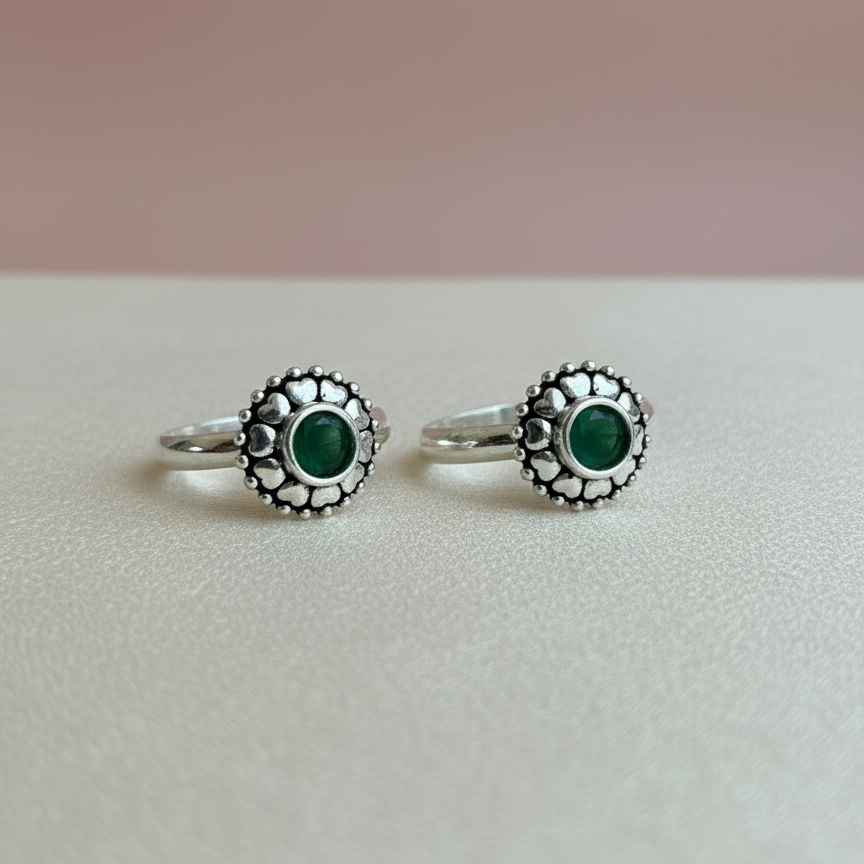 Pair of silver rings with green gemstones on a light pink background