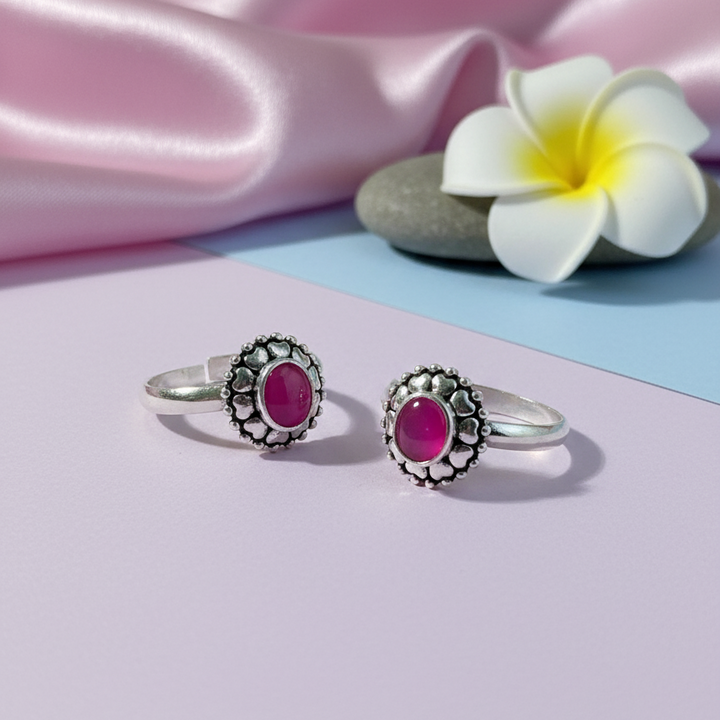 Silver rings with pink gemstones on a pastel background with flowers and fabric.