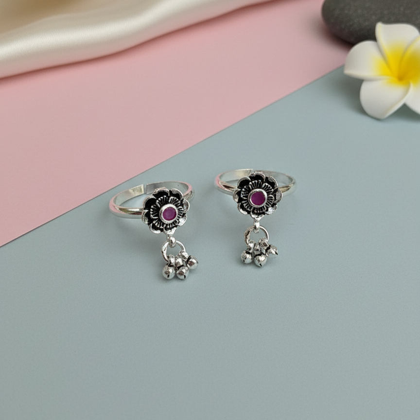 Silver rings with floral designs and gemstones on a pink and gray background.