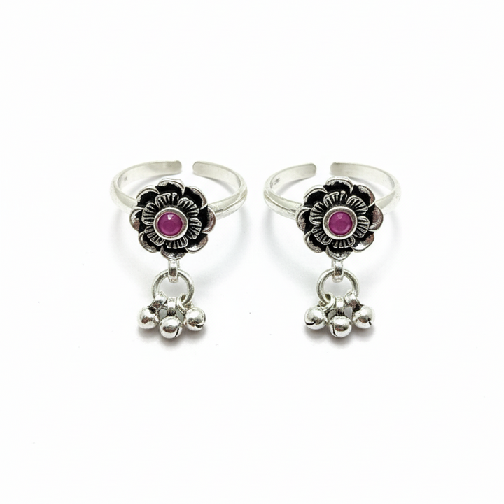 Pair of silver rings with pink gemstones and dangling charms on a white background