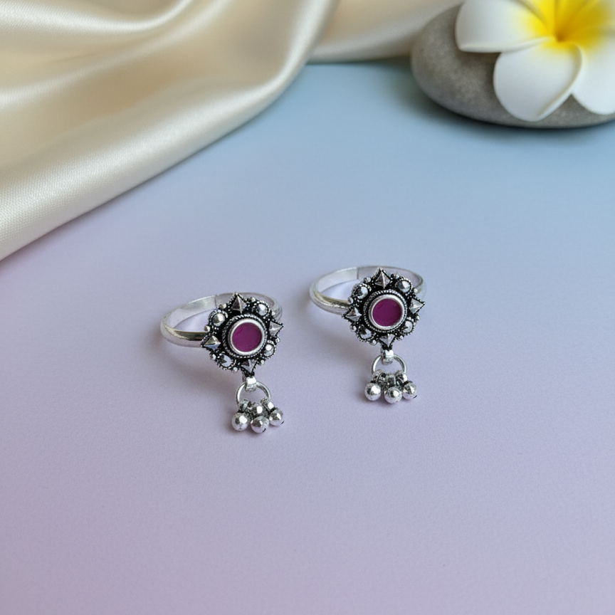 Silver rings with pink gemstones on a light blue surface with a white flower and beige fabric.