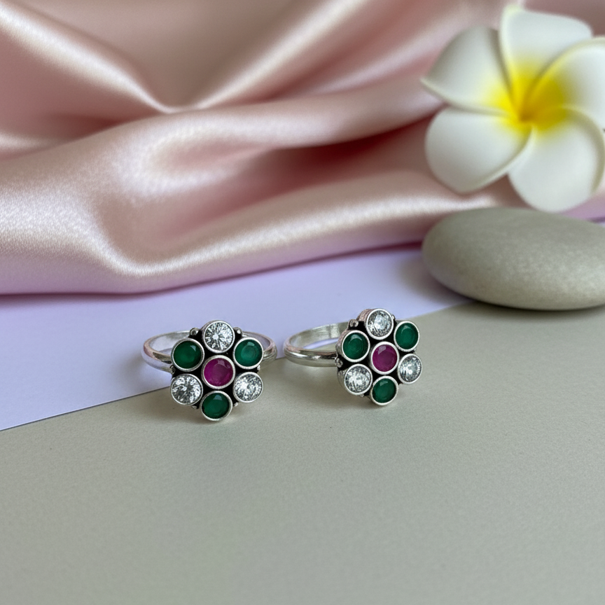 Pair of floral earrings with gemstones on a pink satin fabric background.