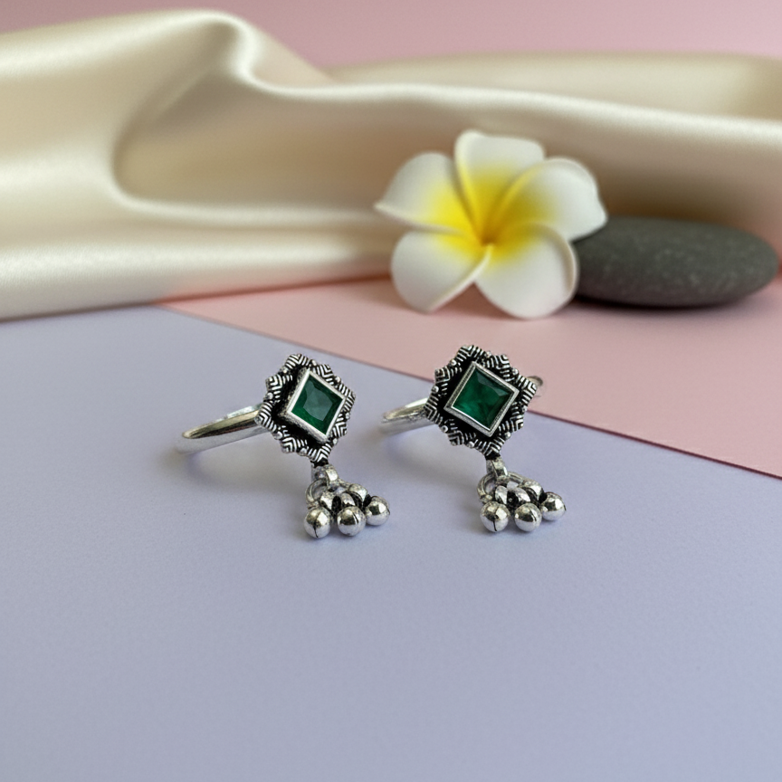 Pair of silver rings with green gemstones on a pink and gray background with a flower.
