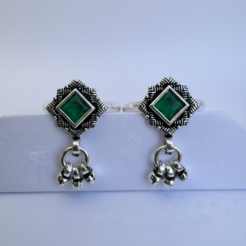 Pair of earrings with green gemstones and silver accents on a light blue background