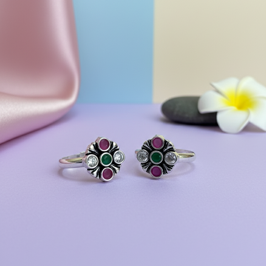Pair of floral silver rings with colored stones on a pastel background